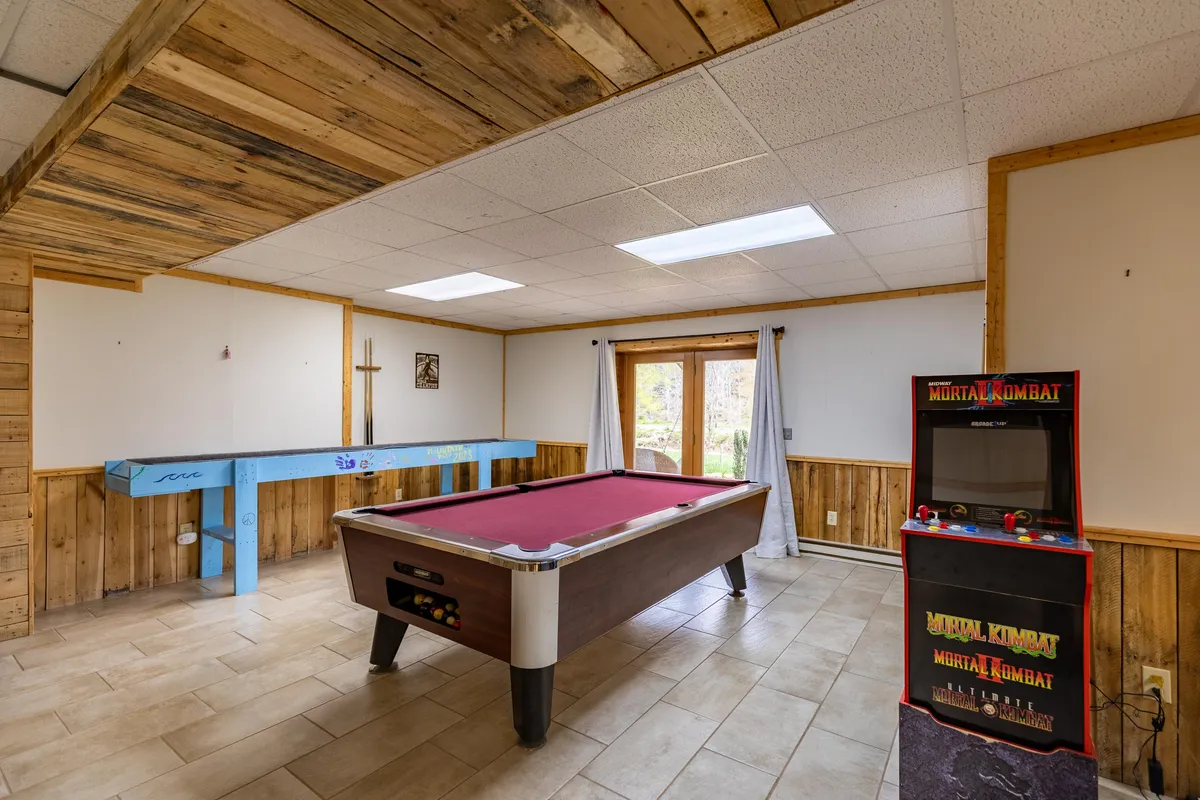 This vibrant interior image showcases the entertainment hub’s heart: a pool table front and center, an arcade cabinet along the wall, and a blue table nearby. The space is brightly lit, exuding a lively, playful atmosphere perfect for group games and casual fun.