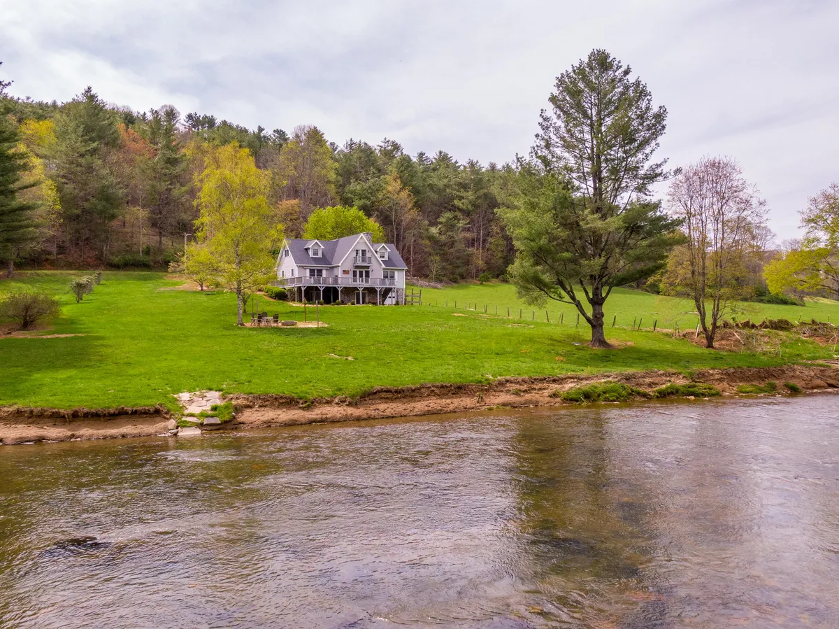 This image displays the house nestled beside the river, framed by trees and natural landscape. The tranquil water and lush greenery evoke a sense of seasonal change, while the proximity to the river hints at activities like fishing, picnicking, or simply relaxing and savoring the view in any season.