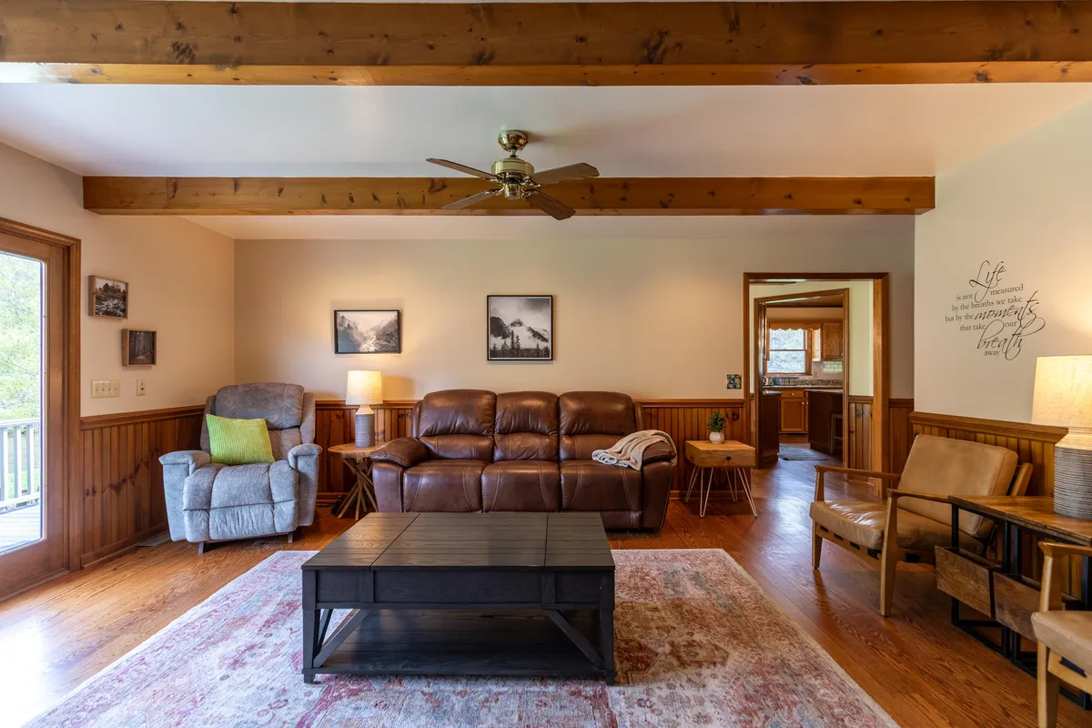 A comfortable living area featuring a leather sofa, wooden coffee table, recliner chair, and table lamp. The arrangement is cozy and inviting, ideal for both socializing and quiet relaxation, reflecting the flexibility of the entertainment space, including the queen sleeper sofa mentioned.