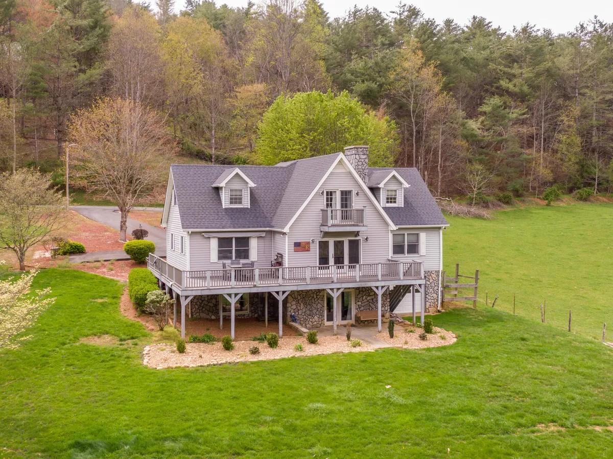 Here, the large front porch of the house is highlighted amidst a manicured lawn and tall trees. The inviting porch and sunset lighting evoke moments of morning coffee, evening relaxation, or gathering after a day of mountain exploring.