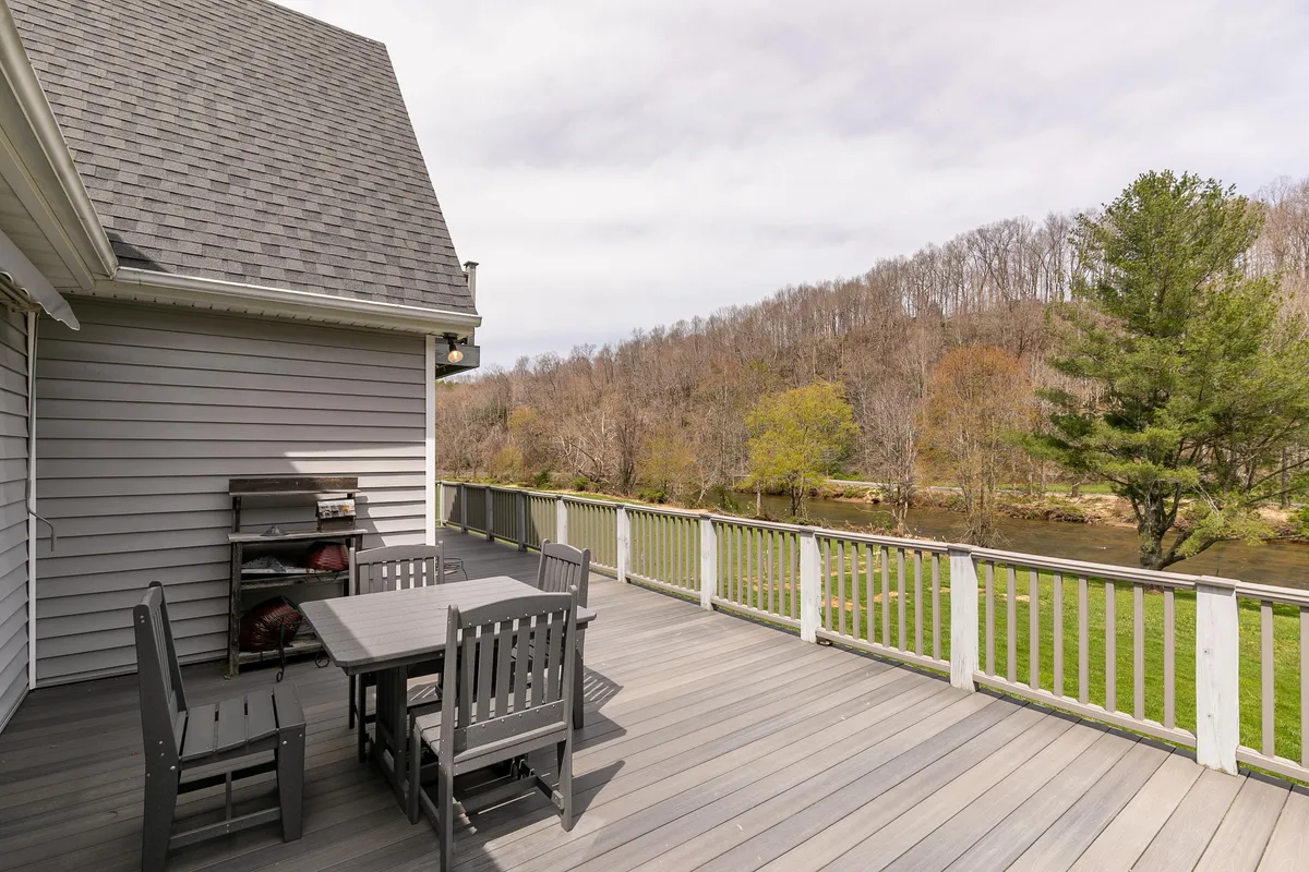 This image captures a serene river view from a deck furnished with comfortable outdoor seating, surrounded by lush trees. The inviting setup is ideal for socializing, enjoying coffee, or simply relaxing and taking in the natural scenery.