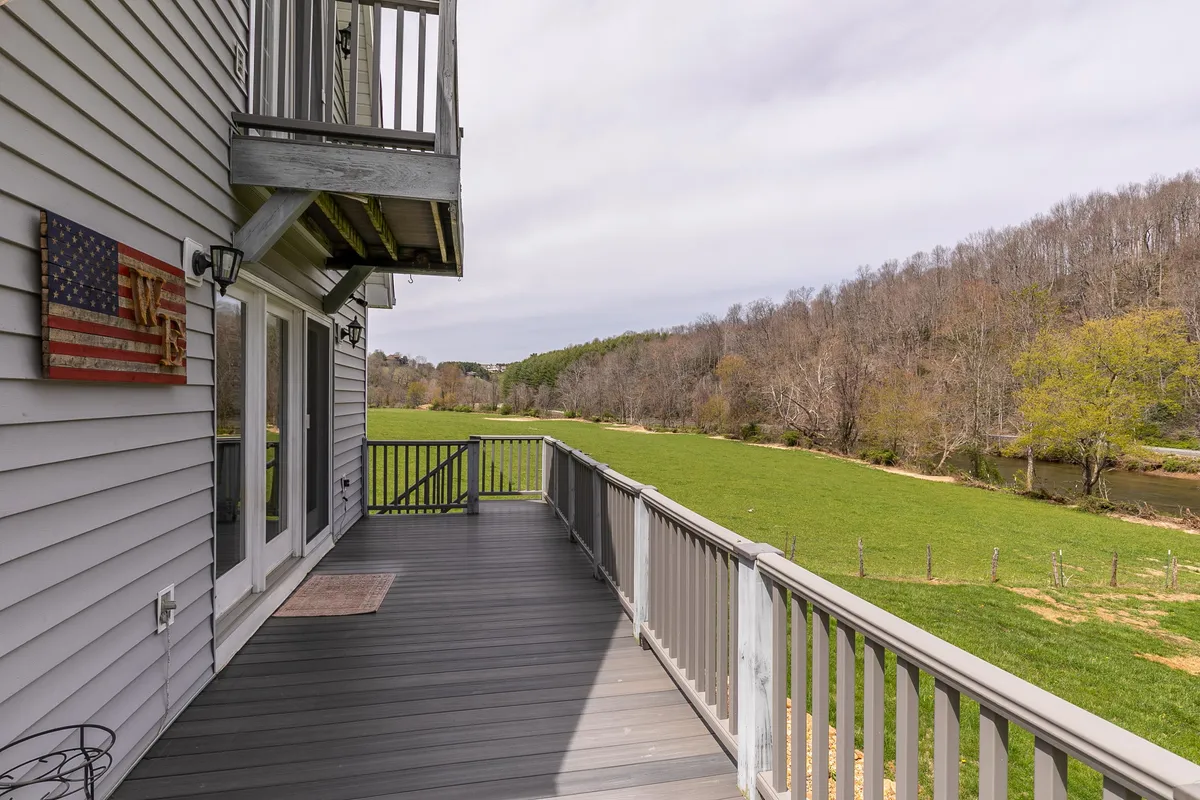 Taken from a deck, the image offers a panoramic view across an expansive green field to the river beyond. The foreground includes a sturdy deck railing and a family-sized American flag, giving a sense of space and belonging.